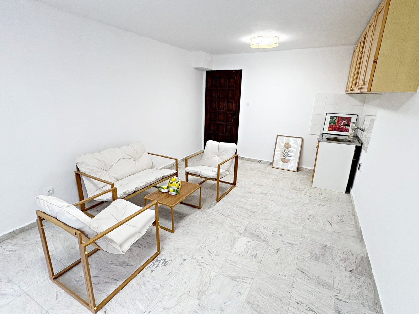 Современная квартира в Болгарии с белыми стенами, мягкой мебелью и кухонным уголком, подходит для покупки или аренды.