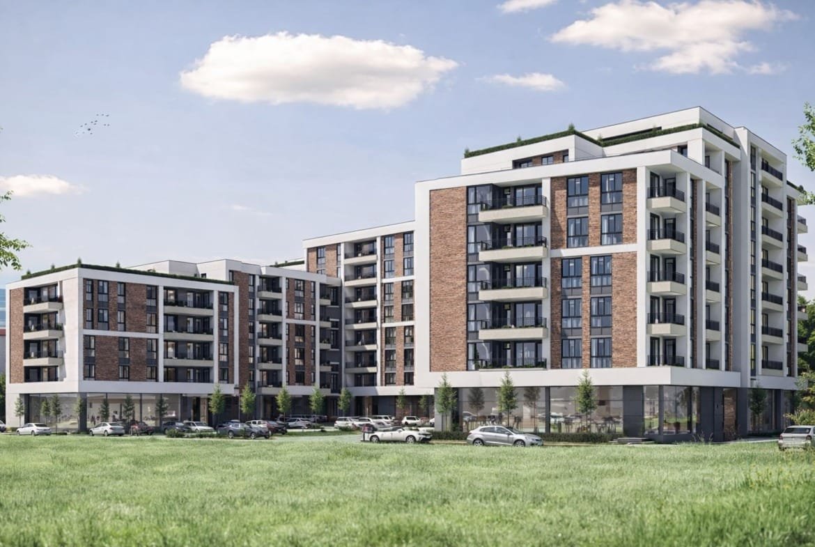 Современный жилой комплекс в Болгарии с кирпичной отделкой и парковкой на фоне зелёного поля и голубого неба.