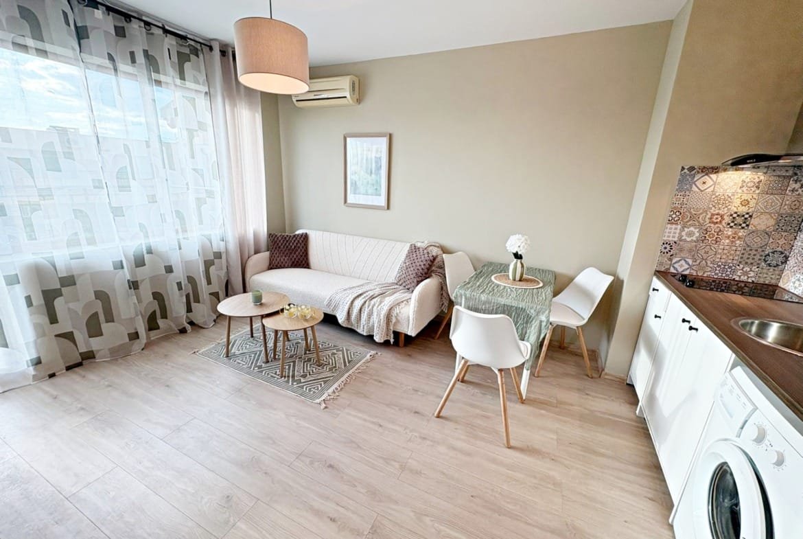 Современный интерьер квартиры в Болгарии с уютной гостиной, столом и кухонным оборудованием. Светлые тона и удобная мебель.