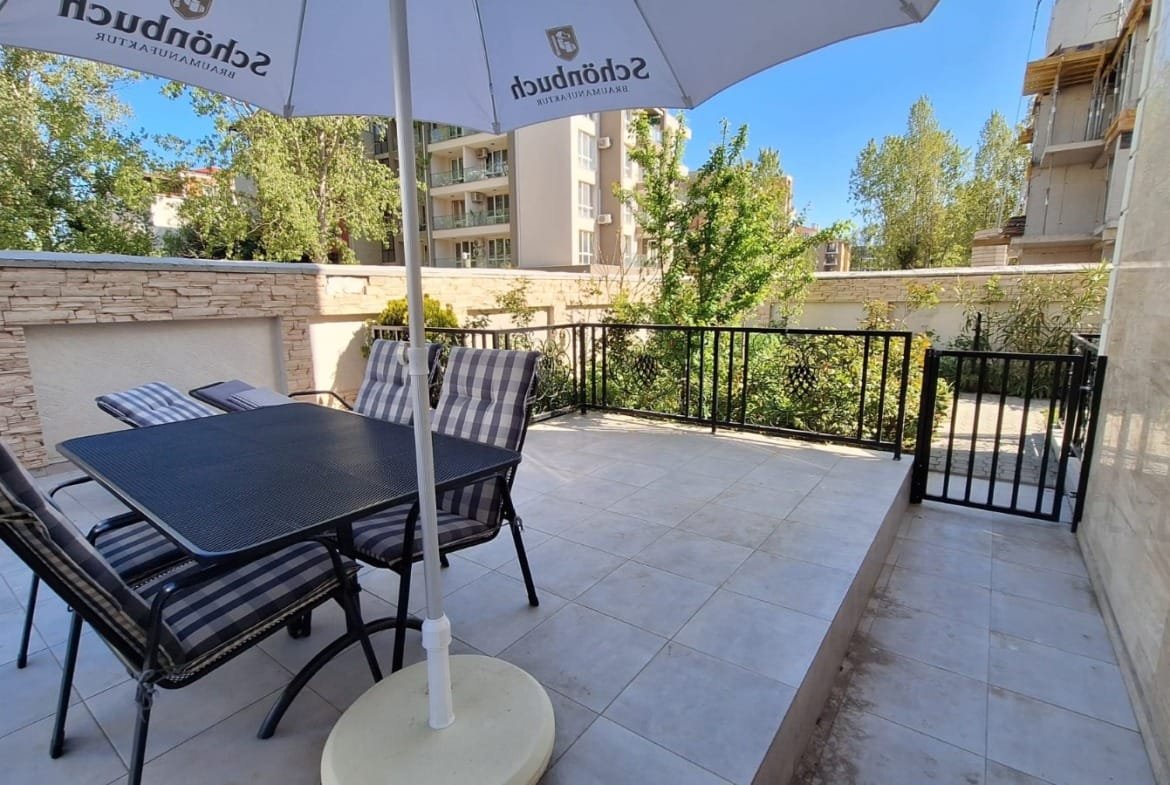 Терраса с площадкой для отдыха, столом и стульями, окруженная зеленью и зданиями в Болгарии, идеальна для продажи недвижимости.