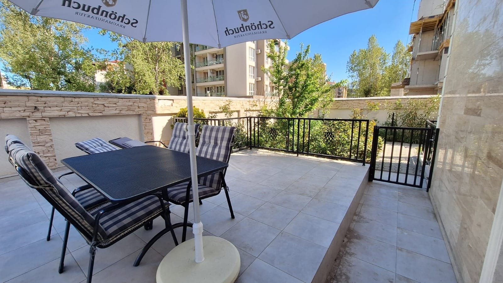 Терраса с площадкой для отдыха, столом и стульями, окруженная зеленью и зданиями в Болгарии, идеальна для продажи недвижимости.