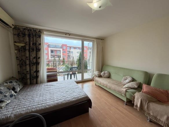 Светлая комната с двуспальной кроватью и зеленым диваном, выходящая на балкон с видом на двор и жилые дома.