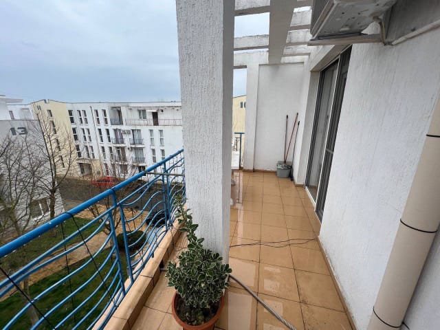 Балкон современной квартиры в Болгарии с видом на жилые здания, плиточным полом и зелёным растением в горшке.