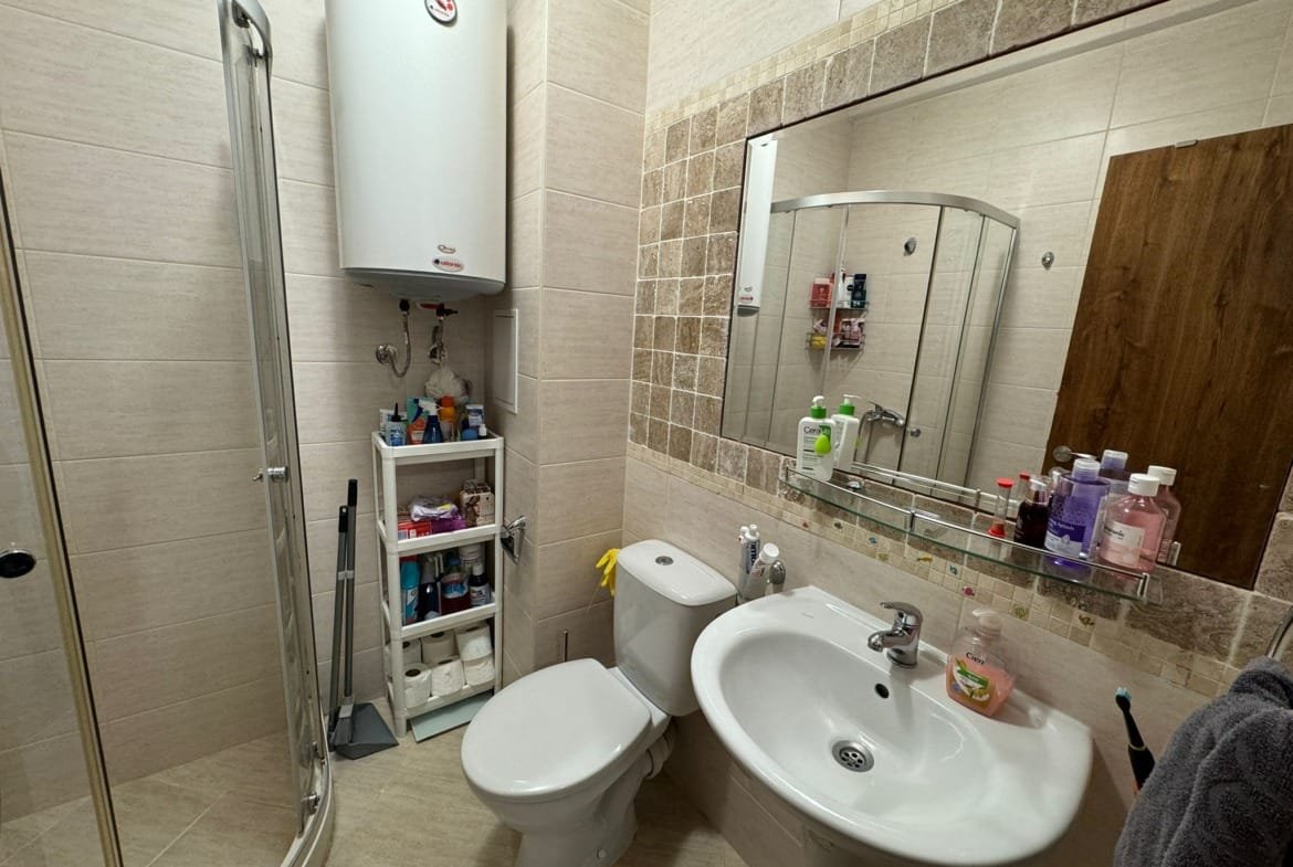 Современная ванная комната с душевой кабиной, умывальником, туалетом и полками для косметических средств.