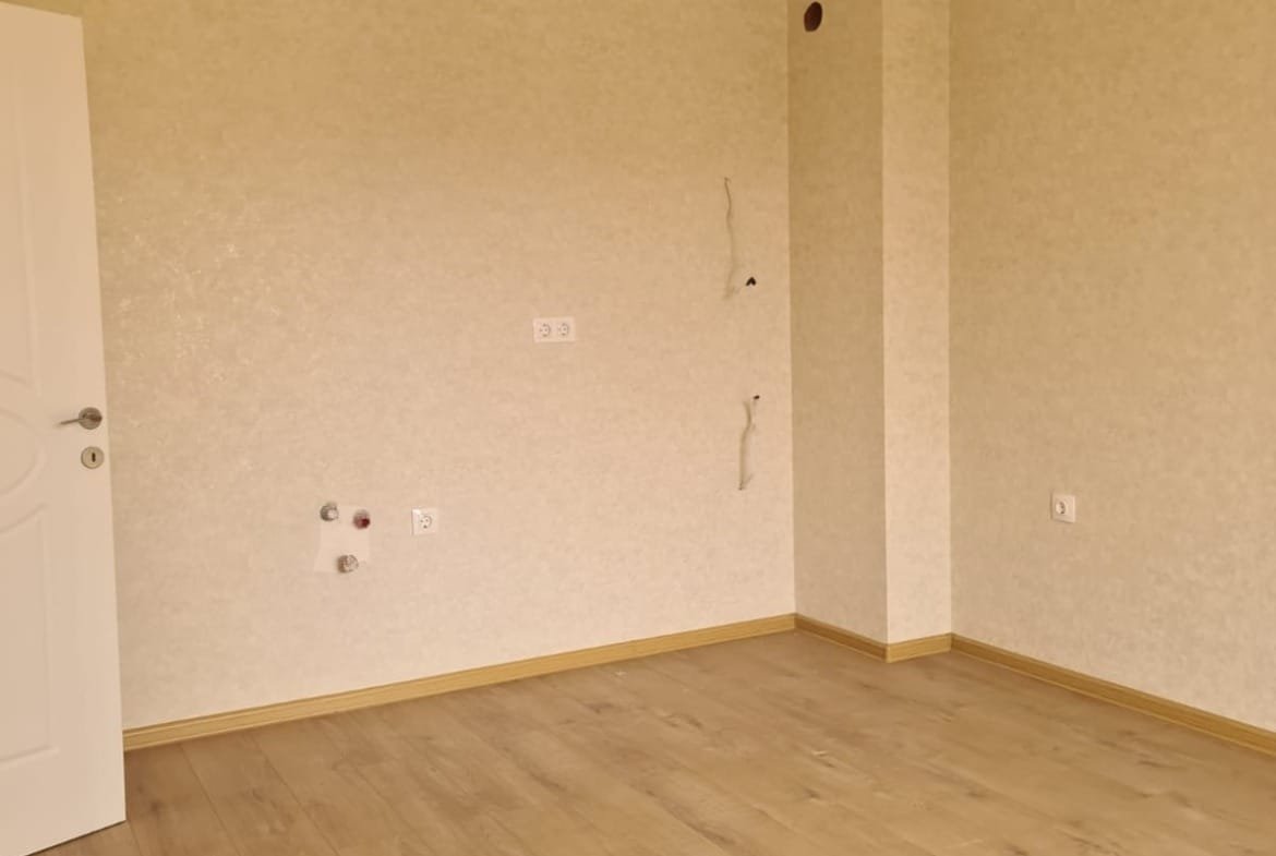 Светлая комната с деревянным полом, пустыми стенами и открытой дверью, идеально подходящая для продажи недвижимости в Болгарии.