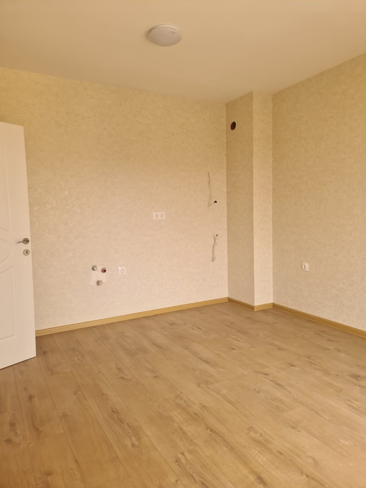 Светлая комната с деревянным полом, пустыми стенами и открытой дверью, идеально подходящая для продажи недвижимости в Болгарии.