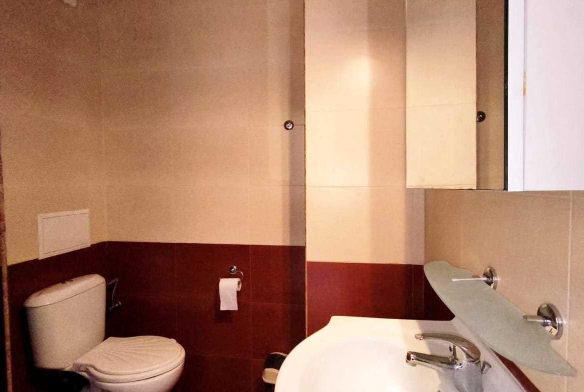 Санузел с белой раковиной и унитазом, стены в бежевых и коричневых тонах, зеркало, светлое освещение.