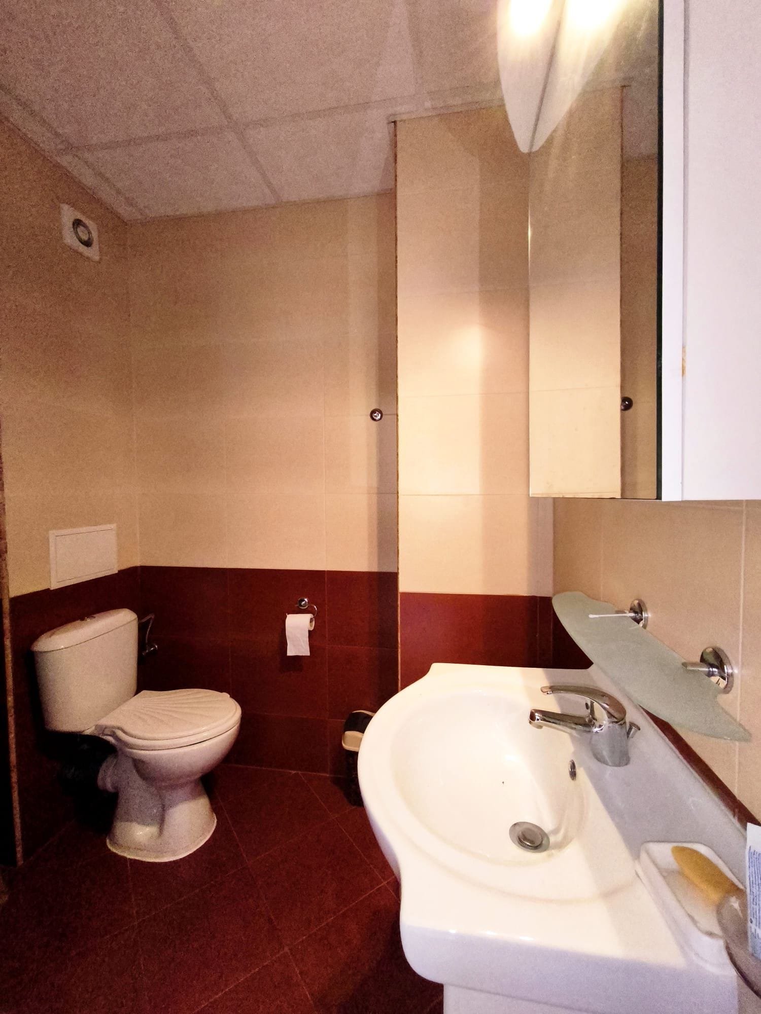 Современный санузел с унитазом и раковиной в нейтральных тонах Санузел с белой раковиной и унитазом, стены в бежевых и коричневых тонах, зеркало, светлое освещение.