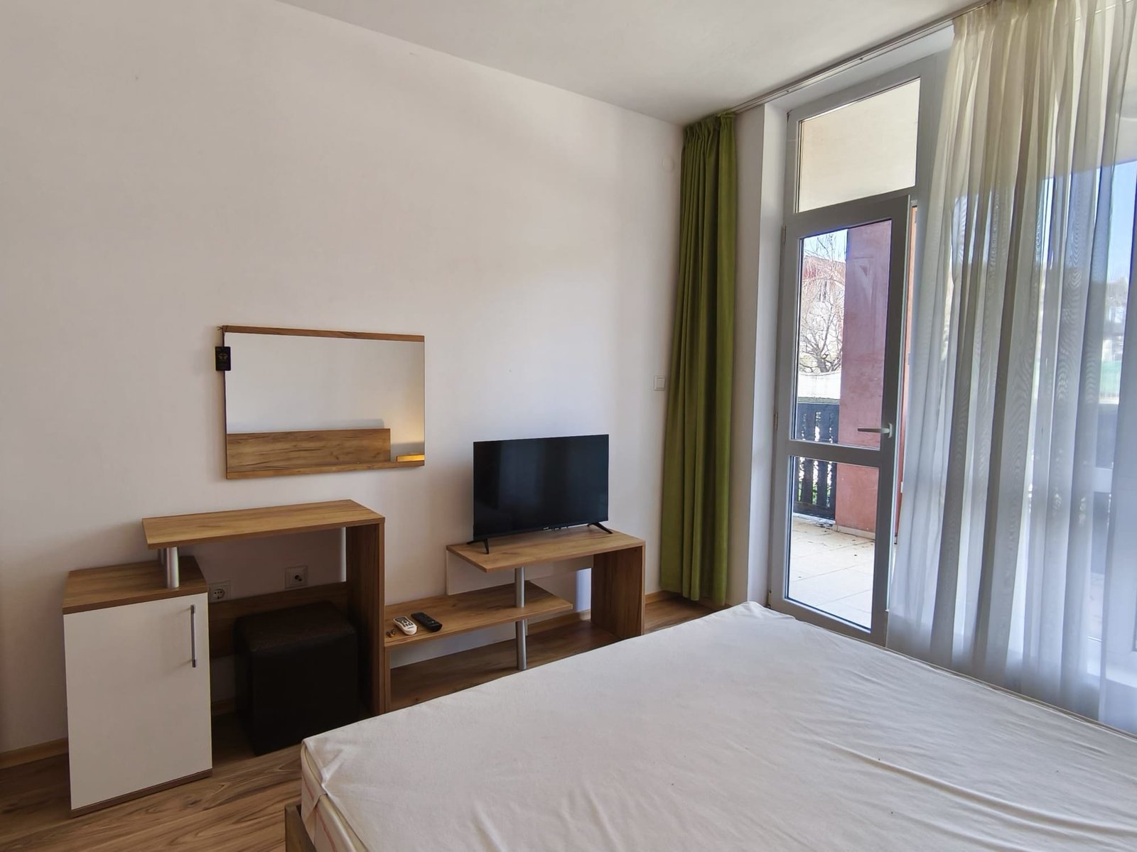 Современная спальня с телевизором и балконом. Современная квартира в Болгарии с уютной спальней, телевизором и балконными дверями, оформленная в светлых тонах.