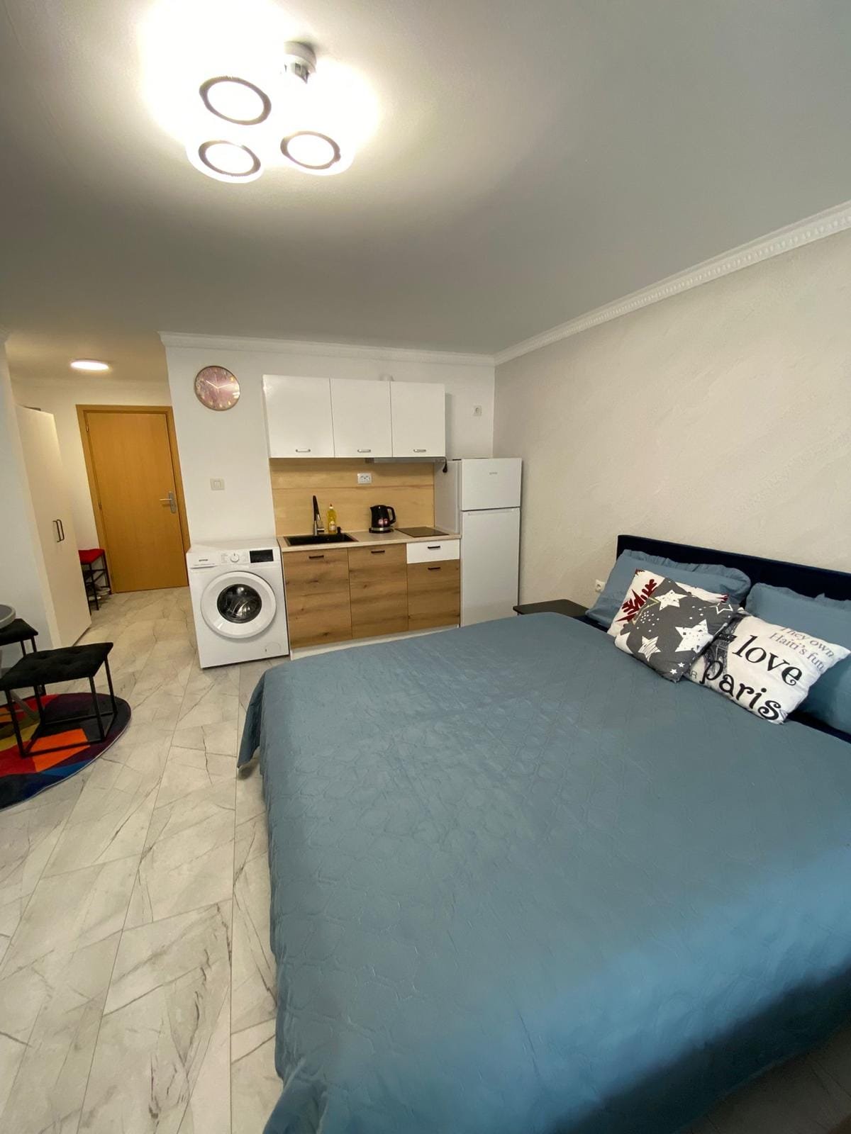 Современная студия с кухонной зоной, стиральной машиной и уютной кроватью, идеальная для покупки или аренды в Болгарии.