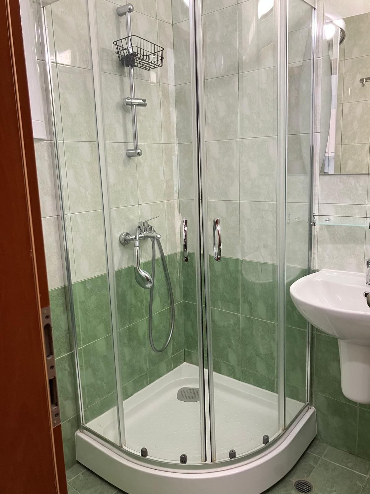 Душевая кабина с прозрачными стеклянными дверцами, зеленая плитка на стенах и раковина с зеркалом в ванной комнате.