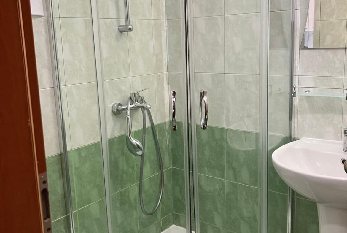 Современная душевая кабина с прозрачными дверцами, плитка светлых тонов, мраморные элементы, оформленный санузел в Болгарии.