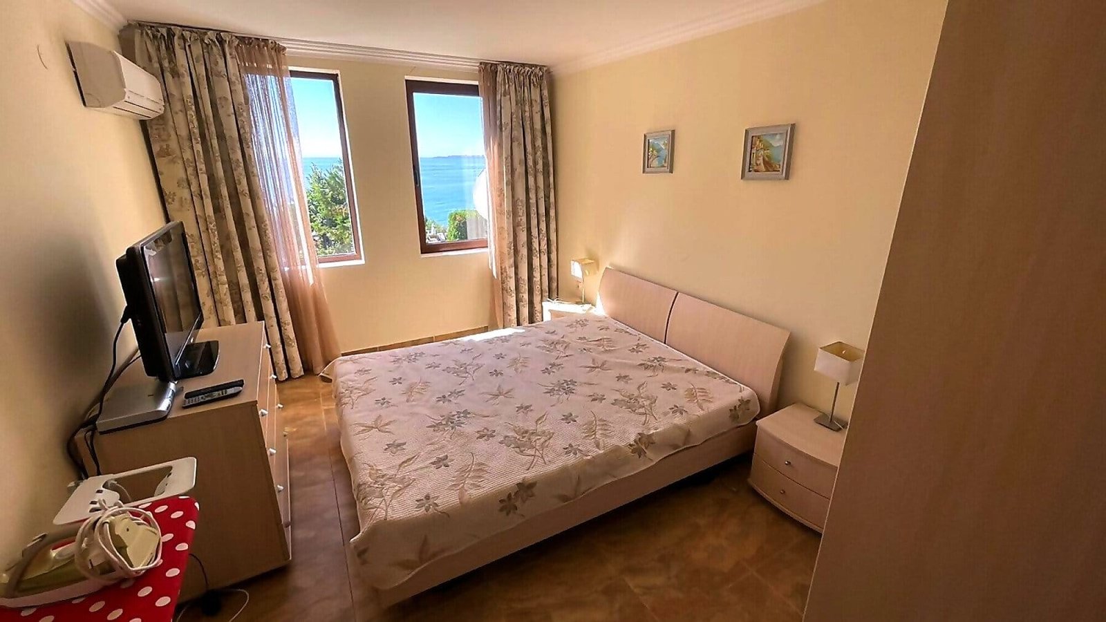 Современная спальня с двуспальной кроватью и видом на море, стены светлых тонов, уютная атмосфера для отдыха в Болгарии.