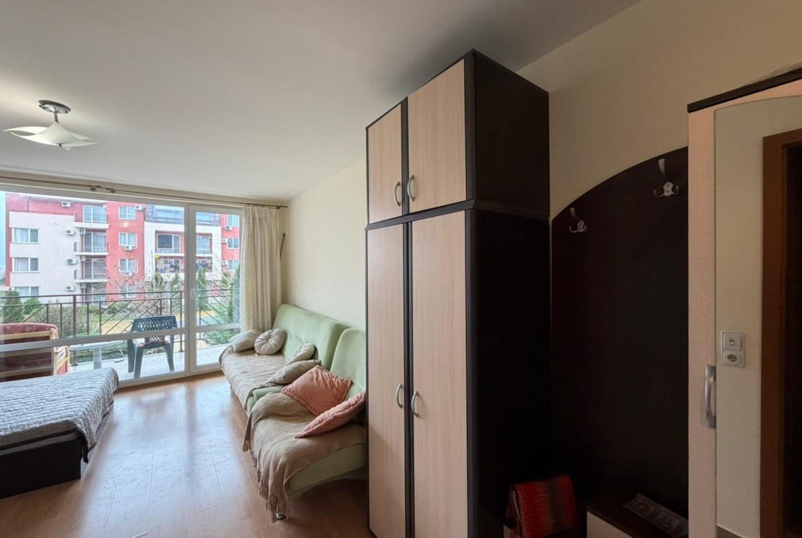 Современная квартира в Болгарии с мебелью, светлыми стенами и панорамным окном, создающим уютную атмосферу.