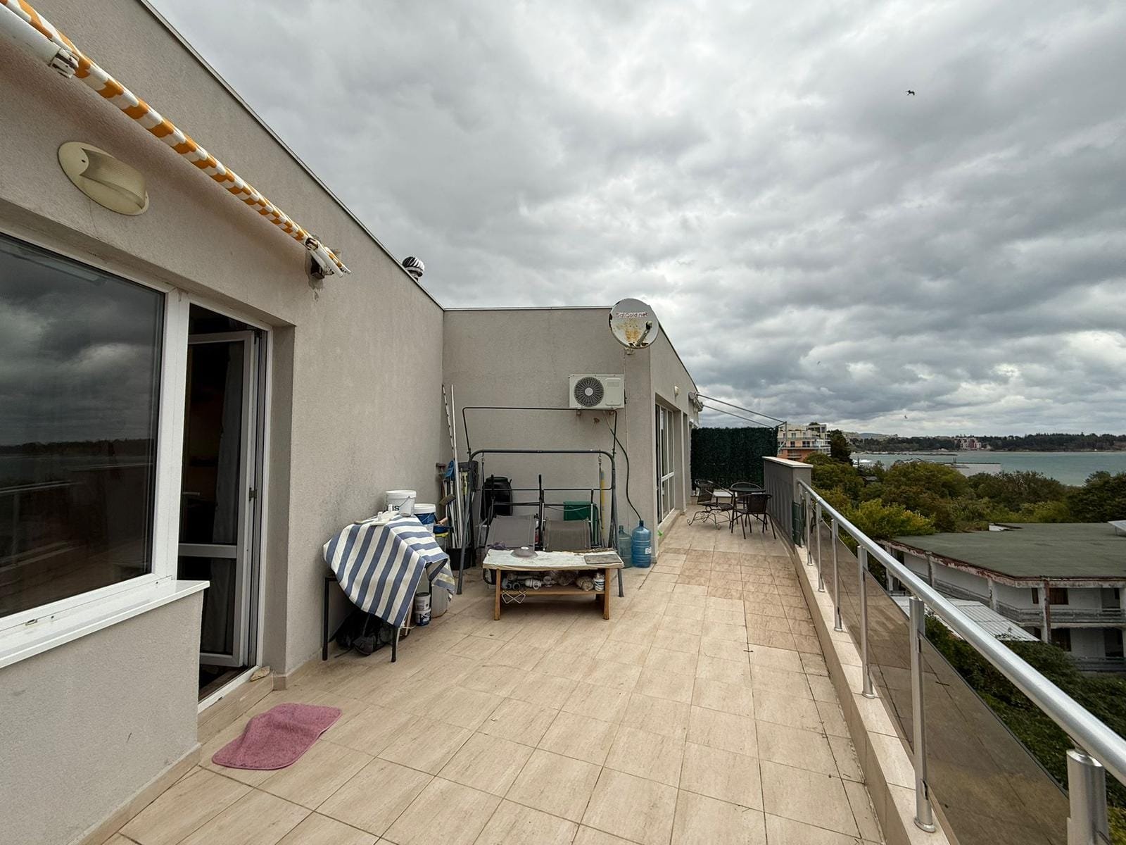 Терраса с шикарным видом на море в Болгарии, оборудованная мебелью и зоной для отдыха, идеальна для покупки недвижимости.