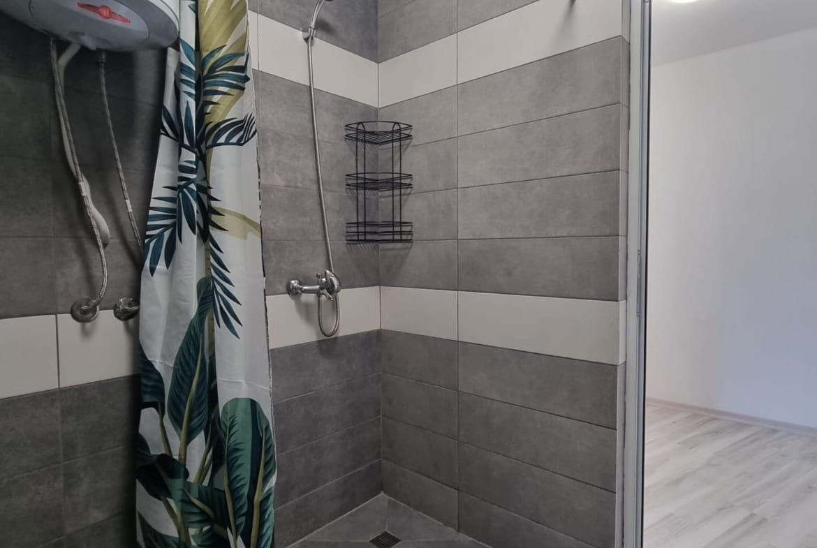 Душевая кабина с современным дизайном, плитка серого цвета, потолочный светильник и занавеска с растительным принтом.