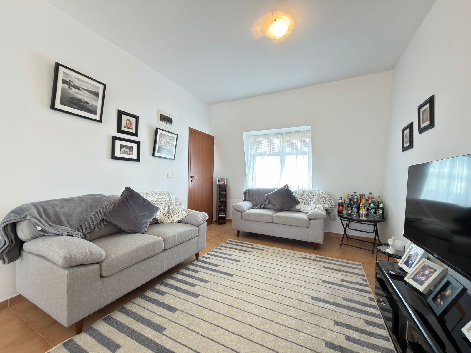 Гостиная с двумя диванами, декоративными рамками на стенах и телевизором, оформленная в нейтральных тонах для продажи недвижимости в Болгарии.