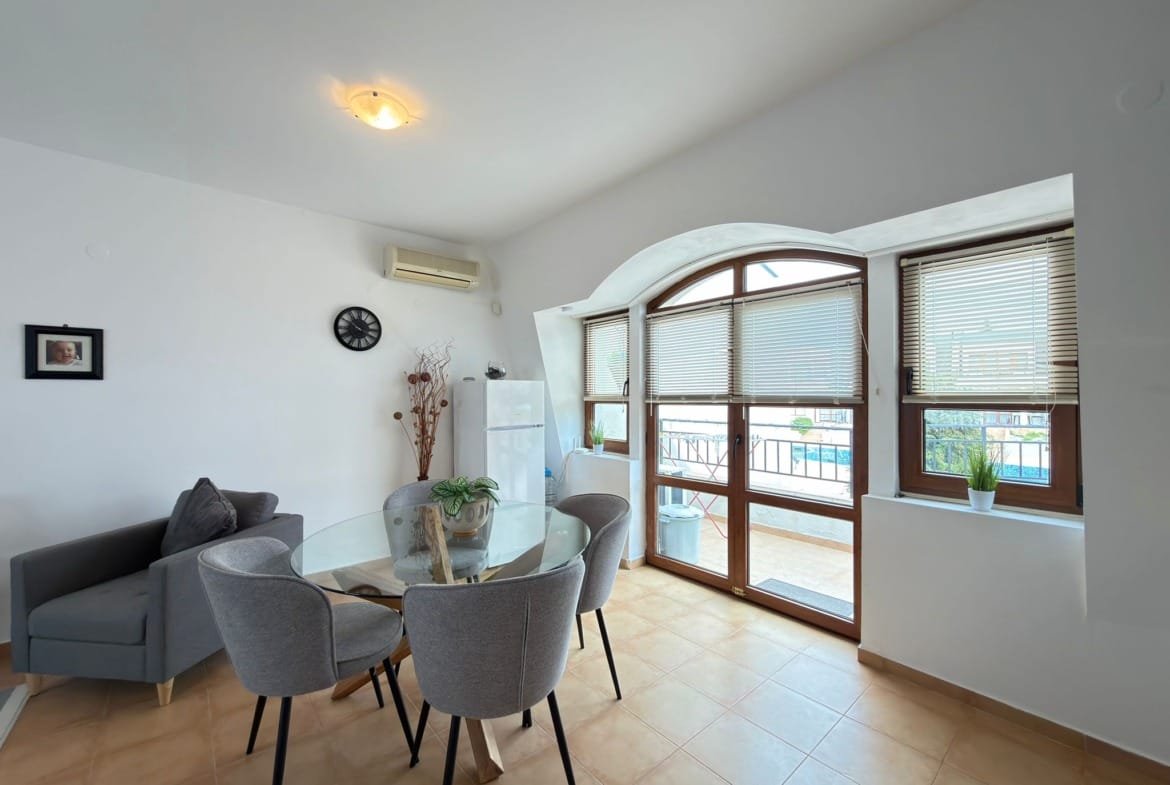 Современная квартира в Болгарии с обеденной зоной, большими окнами и видом на бассейн. Идеальное место для покупки недвижимости.