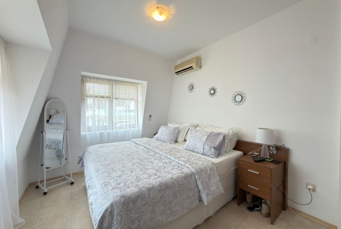 Светлая спальня с двуспальной кроватью, комодом и окном, оформленная в современном стиле, подходит для отдыха в Болгарии.