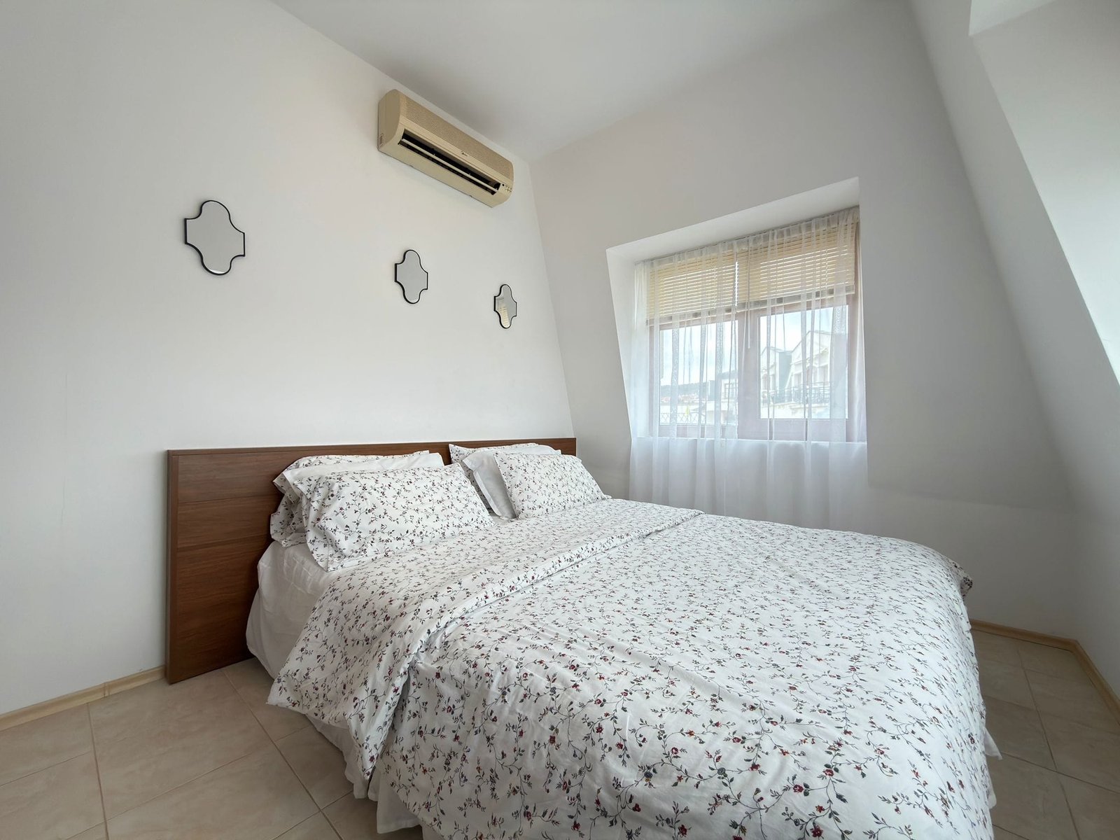 Уютная спальня с двуспальной кроватью и светлыми шторами, идеальная для покупки недвижимости в Болгарии.