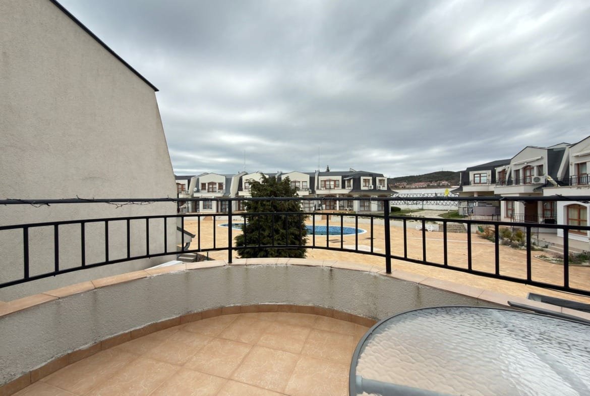 Балкон с видом на жилой комплекс в Болгарии, окружённый зеленью и площадкой у бассейна для отдыха и развлечений.