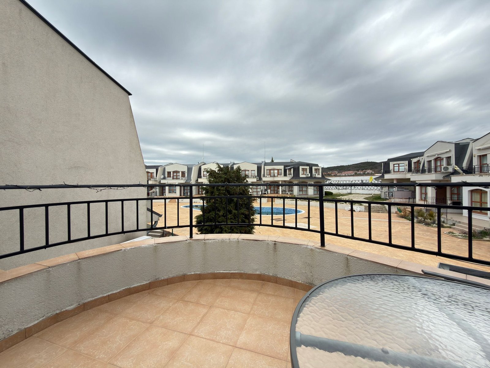 Балкон с видом на жилой комплекс в Болгарии, окружённый зеленью и площадкой у бассейна для отдыха и развлечений.