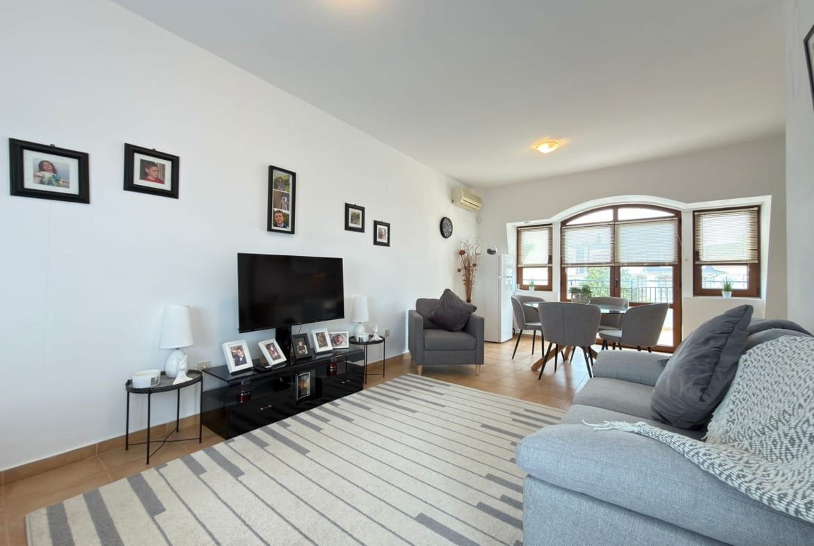 Современный интерьер квартиры в Болгарии с уютной гостиной, телевизором, стульями и декоративными элементами.