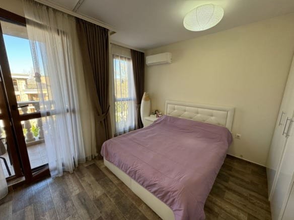 Современная спальня с двуспальной кроватью, балконными дверями и светлыми шторами в жилом доме Болгарии.