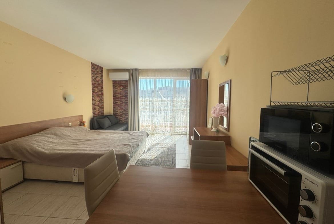 Современная квартира-студия в Болгарии с кухонной зоной, светлым интерьером и балконом, идеальная для продажи и покупки недвижимости.