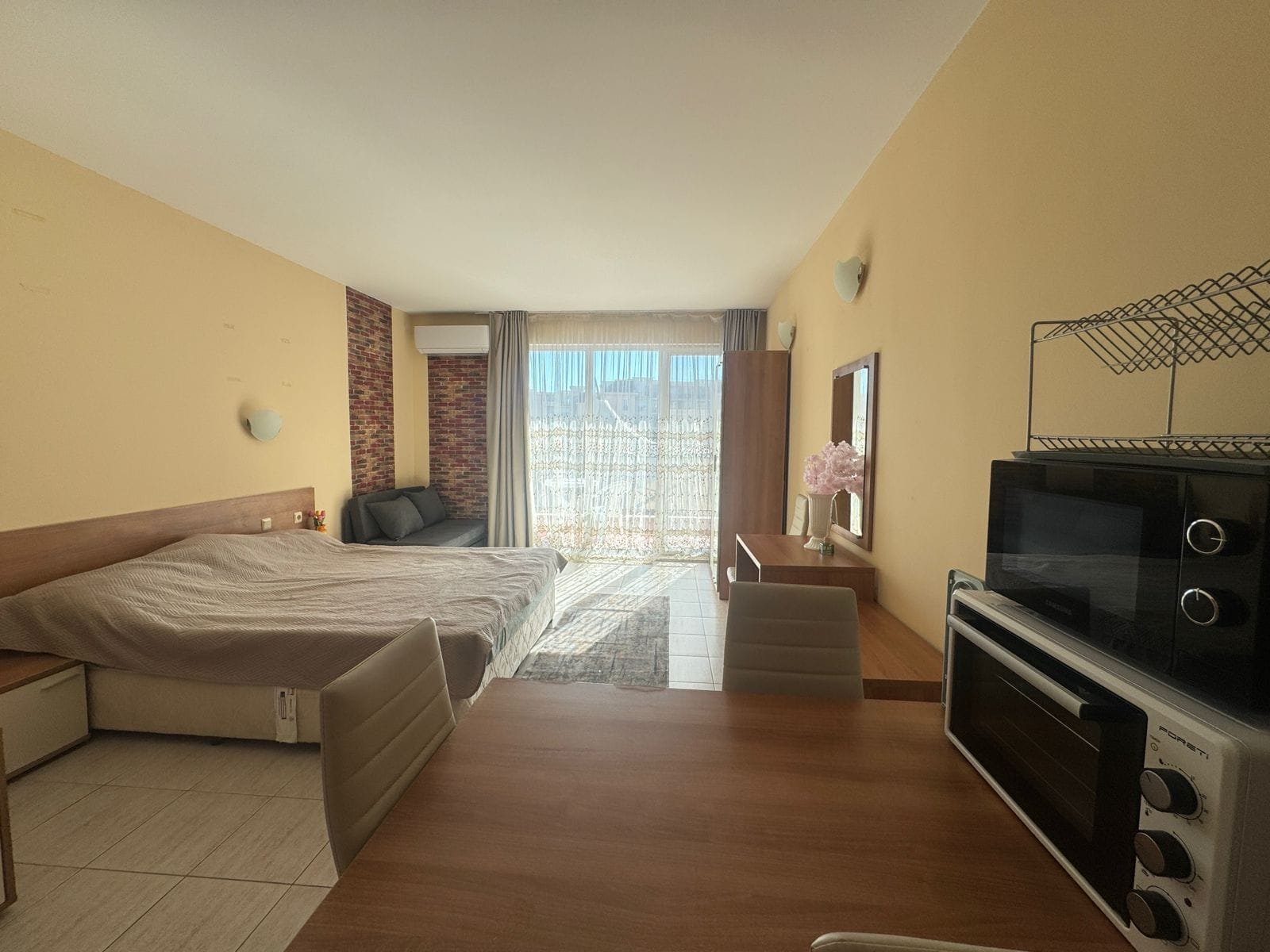 Современная квартира-студия в Болгарии с кухонной зоной, светлым интерьером и балконом, идеальная для продажи и покупки недвижимости.