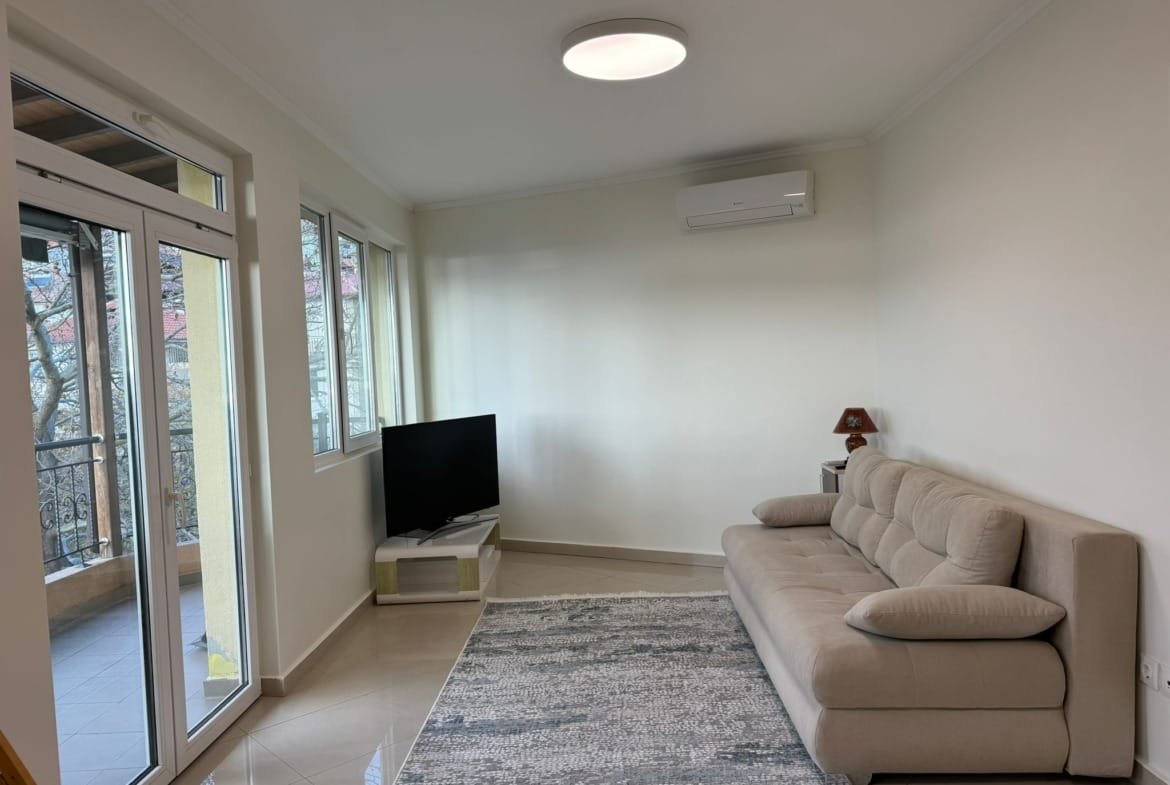 Современная гостиная с диваном, телевизором и светлым интерьером, идеальная для покупки недвижимости в Болгарии.