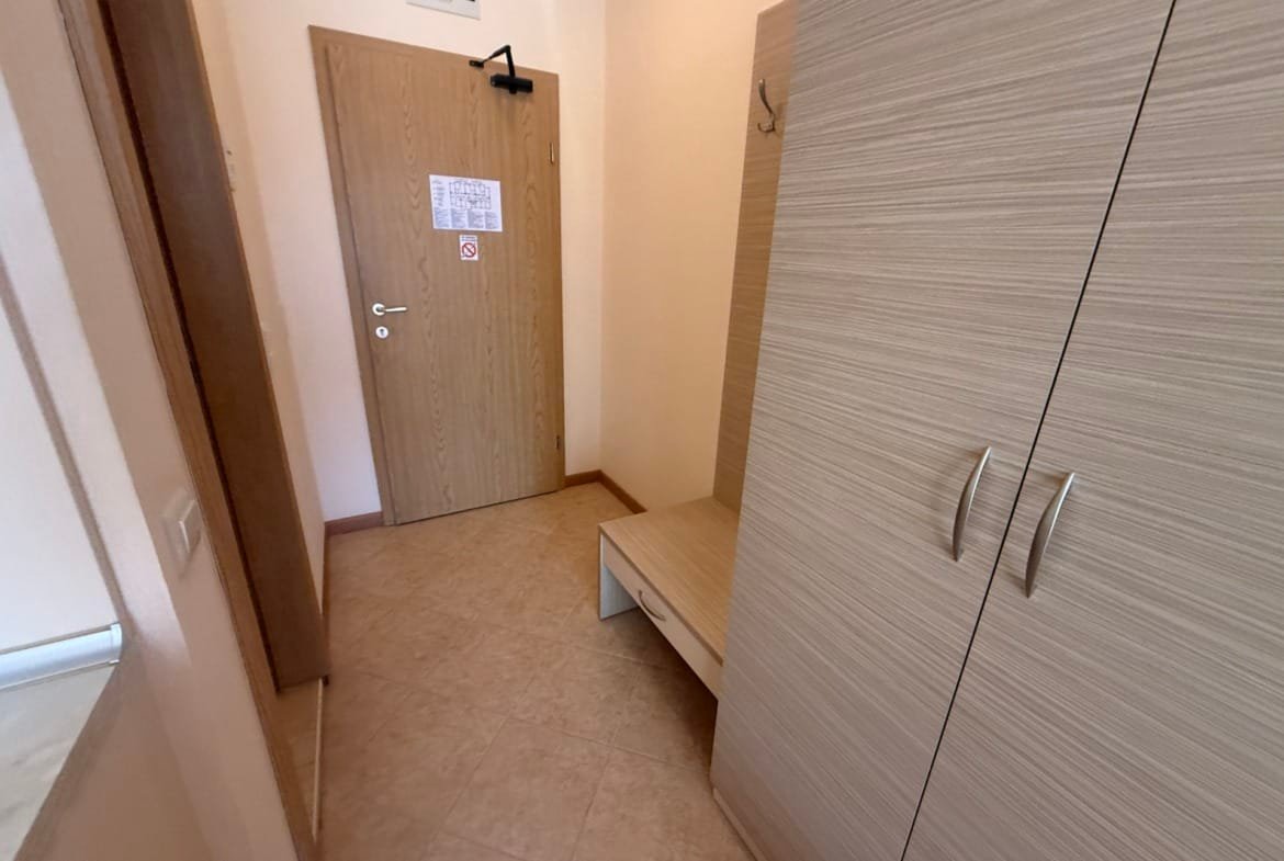 Коридор квартиры с светлыми стенами, шкафом и скамейкой, подходящий для продажи недвижимости в Болгарии.