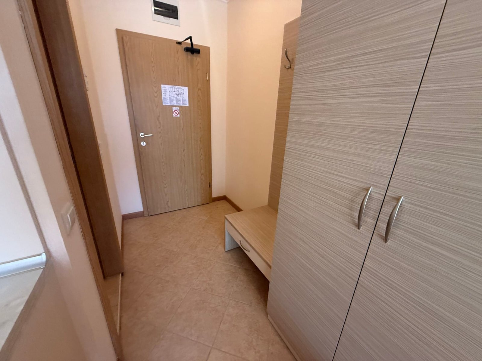 Коридор квартиры с светлыми стенами, шкафом и скамейкой, подходящий для продажи недвижимости в Болгарии.