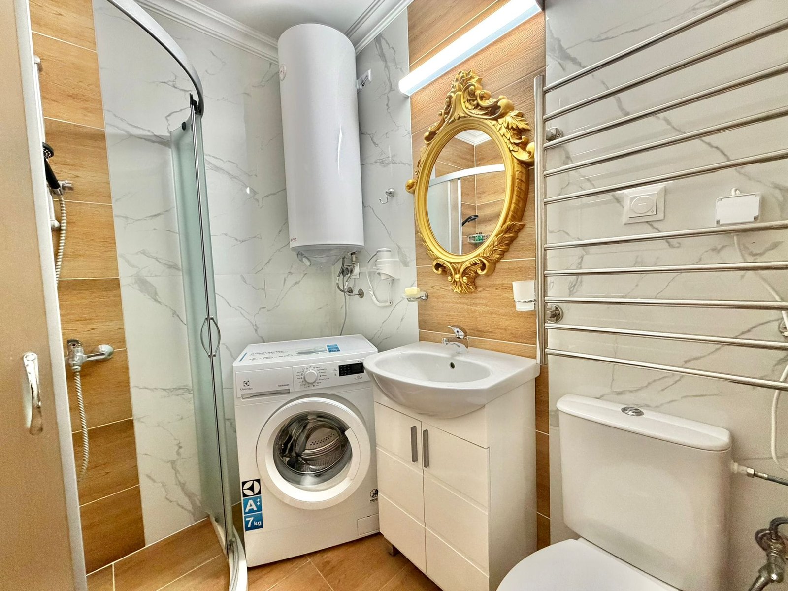 Санузел в квартире с душевой кабиной, стиральной машиной и золотым зеркалом на стене, стильный и современный.