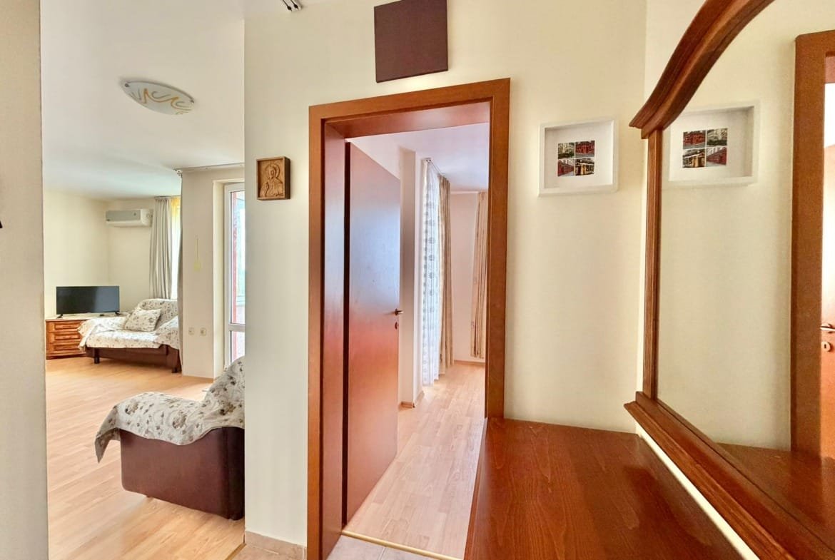 Современный интерьер квартиры в Болгарии с деревянной мебелью, телевизором и светлыми стенами, создающими уютную атмосферу.