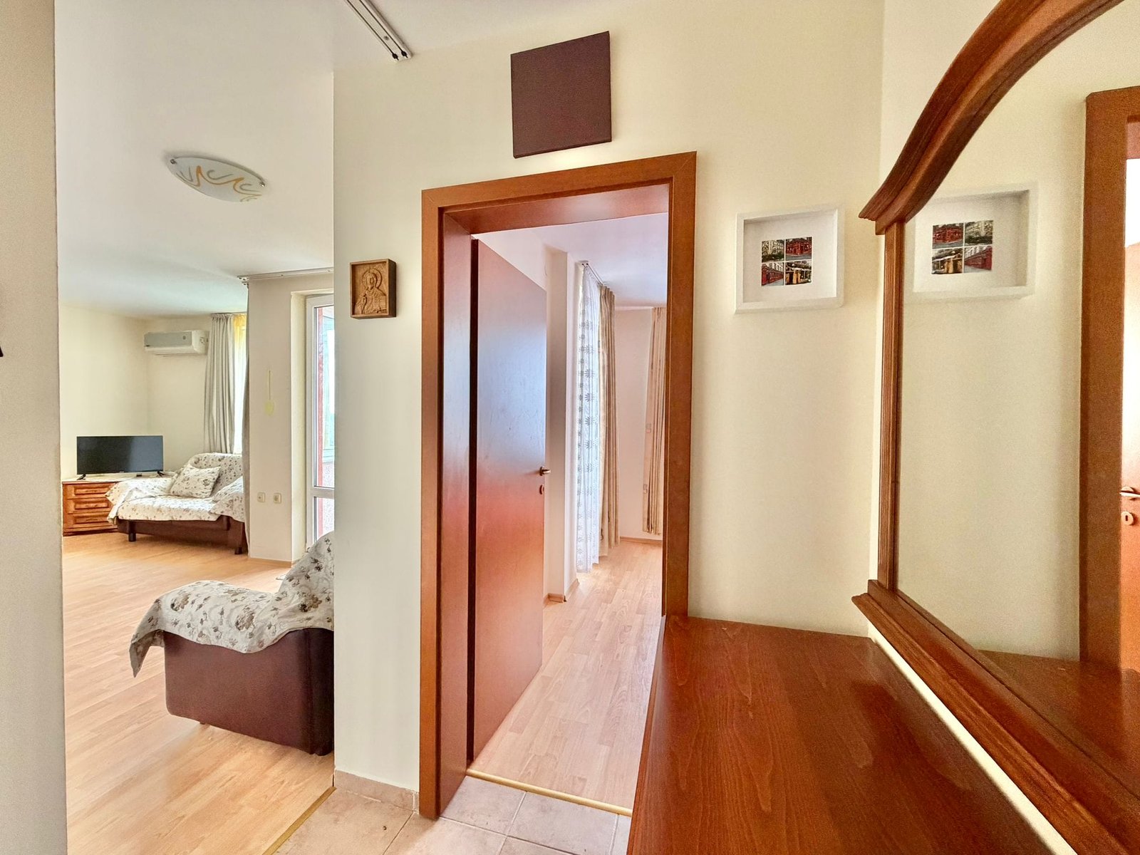 Современный интерьер квартиры в Болгарии с деревянной мебелью, телевизором и светлыми стенами, создающими уютную атмосферу.