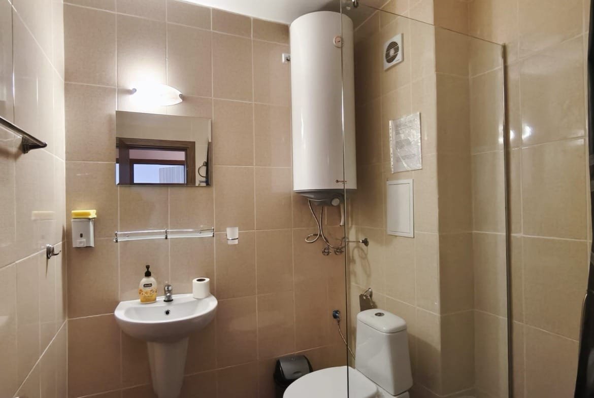 Современная ванная комната с сантехникой, белым унитазом и душевой кабиной, уютная обстановка для жилья в Болгарии.