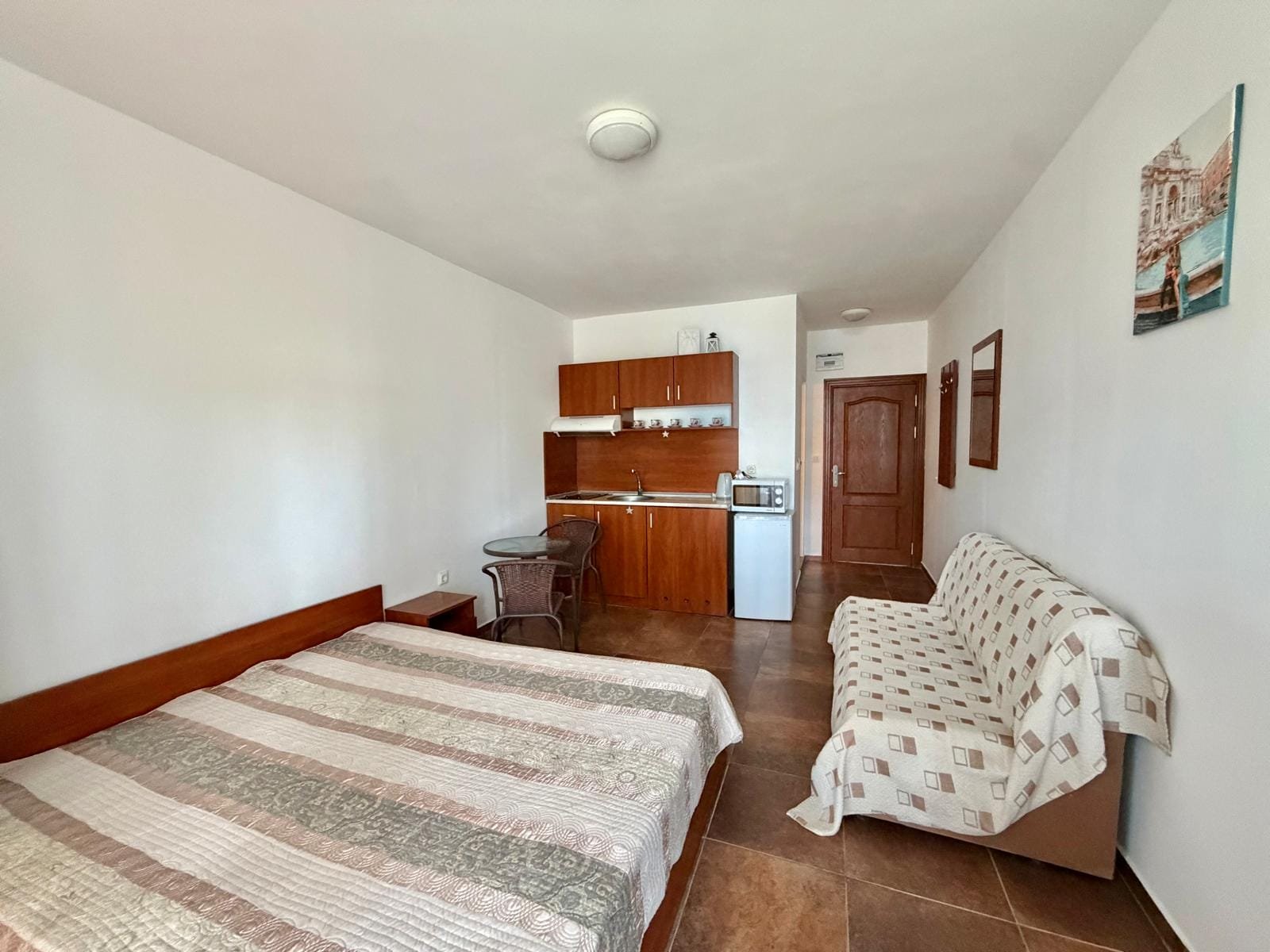 Уютная студия с деревянной мебелью, кухонным уголком и диваном, идеальная для проживания или аренды в Болгарии.