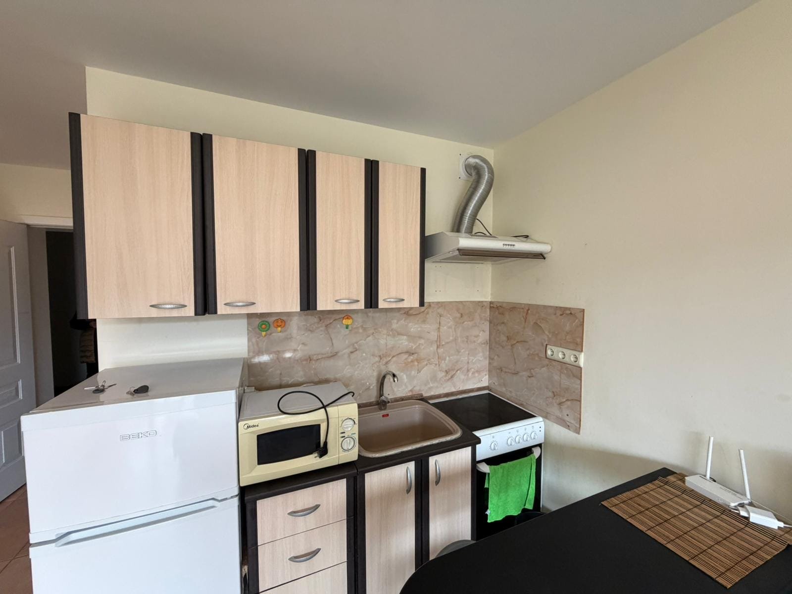 Современная кухня: компактные шкафчики и бытовая техника Современная кухня с холодильником, плитой, микроволновкой и столешницей, идеально подходящая для покупки недвижимости в Болгарии.