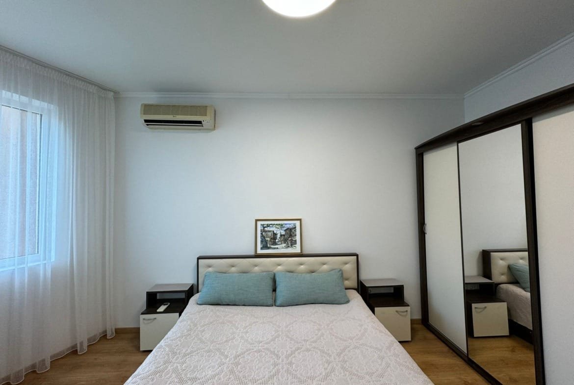 Современная спальня с двуспальной кроватью, светлыми стенами и зеркальным шкафом, идеально подходит для покупки недвижимости в Болгарии.