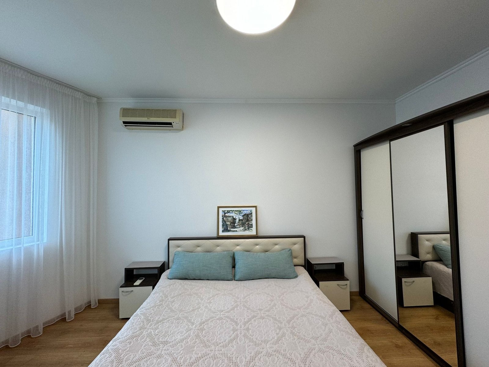 Современная спальня с зеркальным шкафом и светлой отделкой Современная спальня с двуспальной кроватью, светлыми стенами и зеркальным шкафом, идеально подходит для покупки недвижимости в Болгарии.