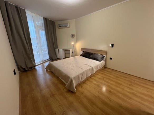 Современная спальня с односпальной кроватью, светлыми стенами и окнами, выходящими на балкон, идеальна для жизни в Болгарии.