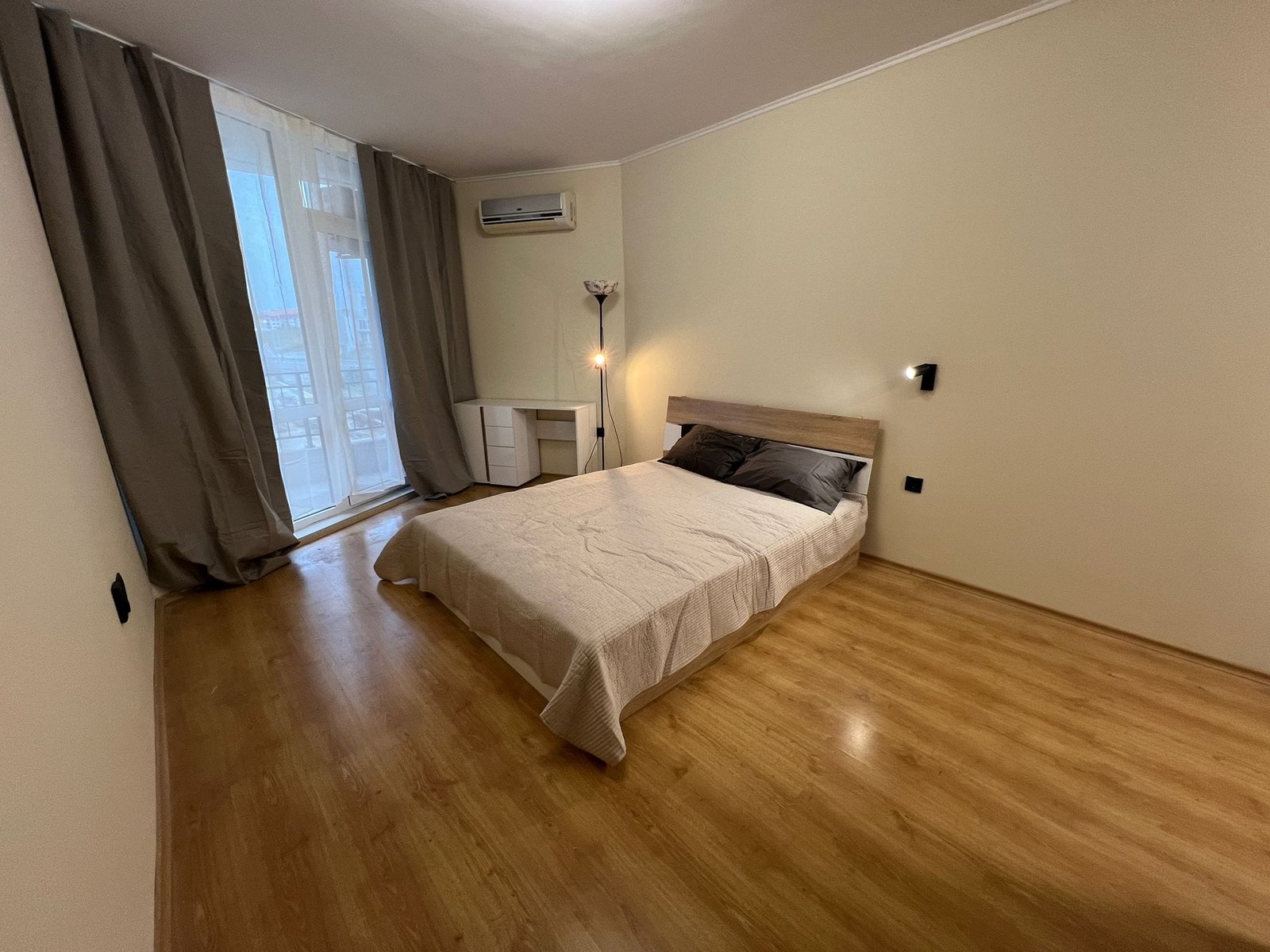 Современная спальня с светлыми тонами и большим окном Современная спальня с односпальной кроватью, светлыми стенами и окнами, выходящими на балкон, идеальна для жизни в Болгарии.