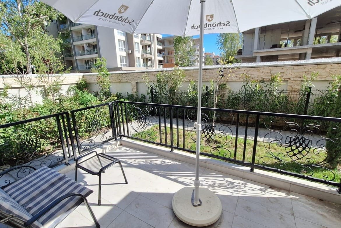 Балкон с зонтом и креслом, выходящий на зелёный сад в жилом комплексе Болгарии, идеальное место для отдыха.