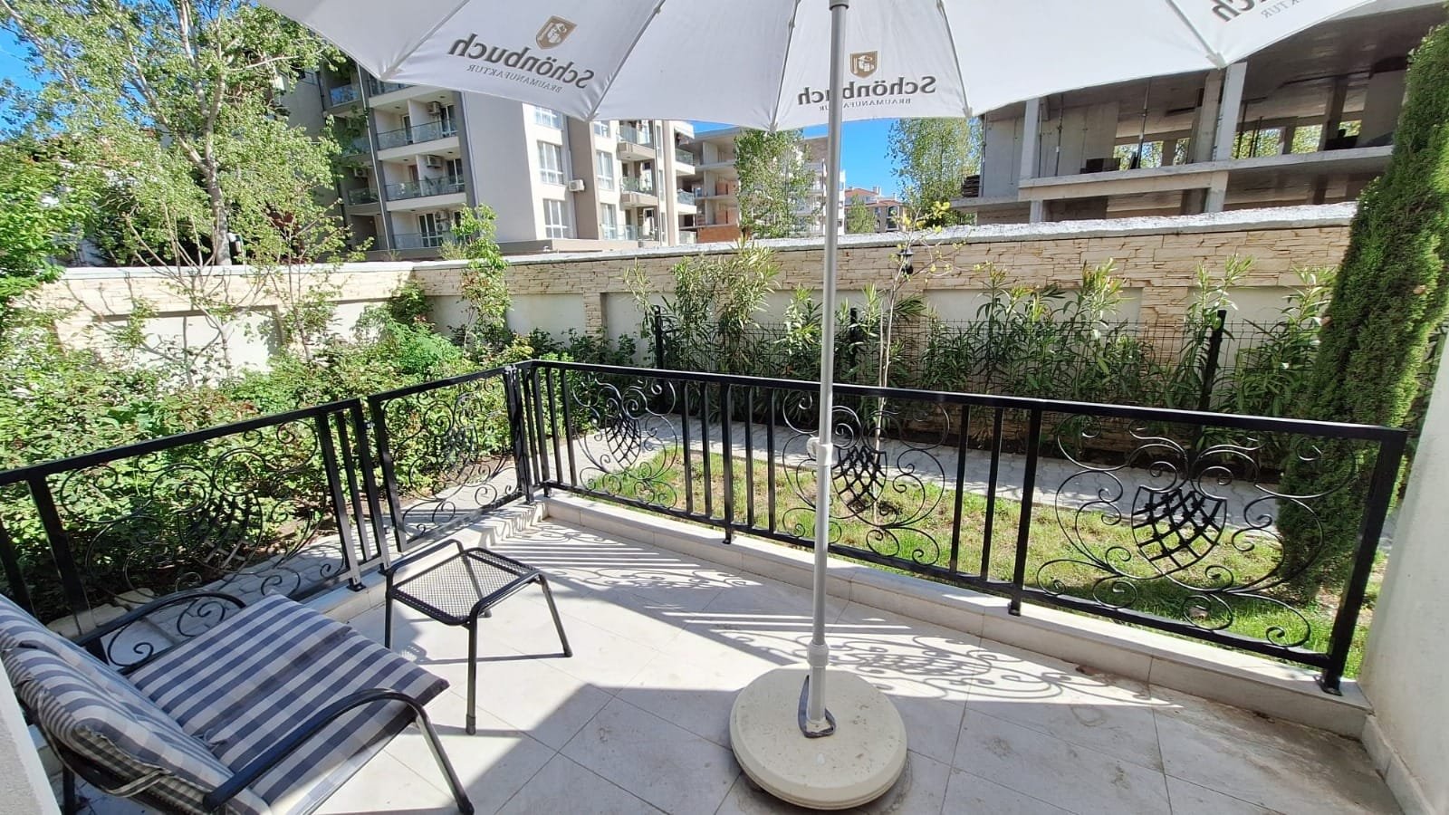 Балкон с зонтом и креслом, выходящий на зелёный сад в жилом комплексе Болгарии, идеальное место для отдыха.