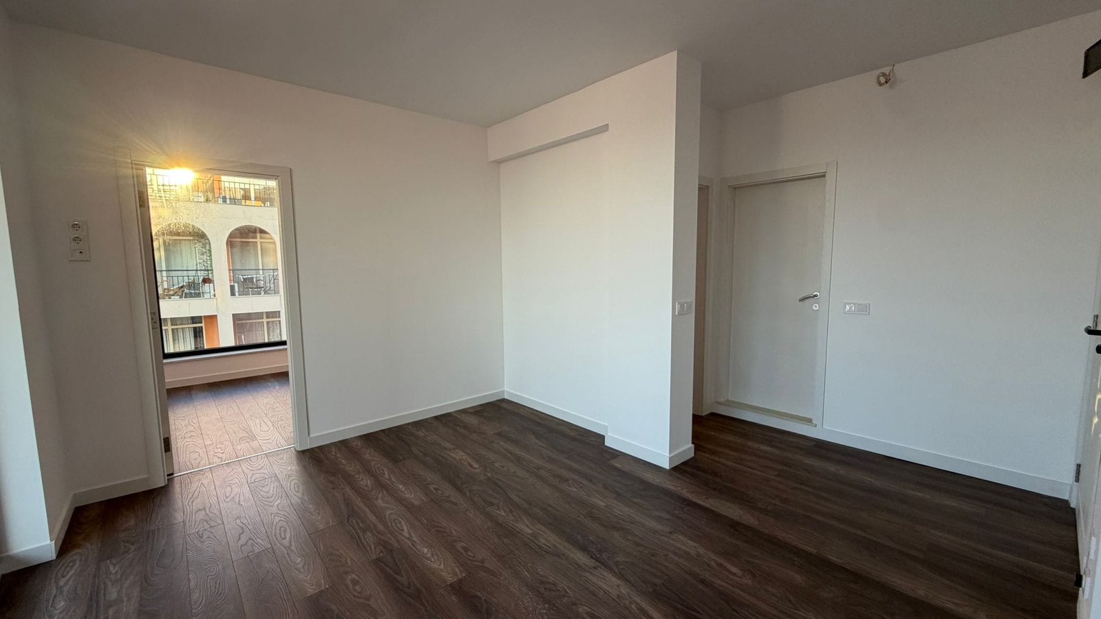 Современный интерьер пустой квартиры с деревянным полом Современная квартира в Болгарии с светлыми стенами, светлым паркетом и выходом на балкон, идеальна для покупки или аренды.