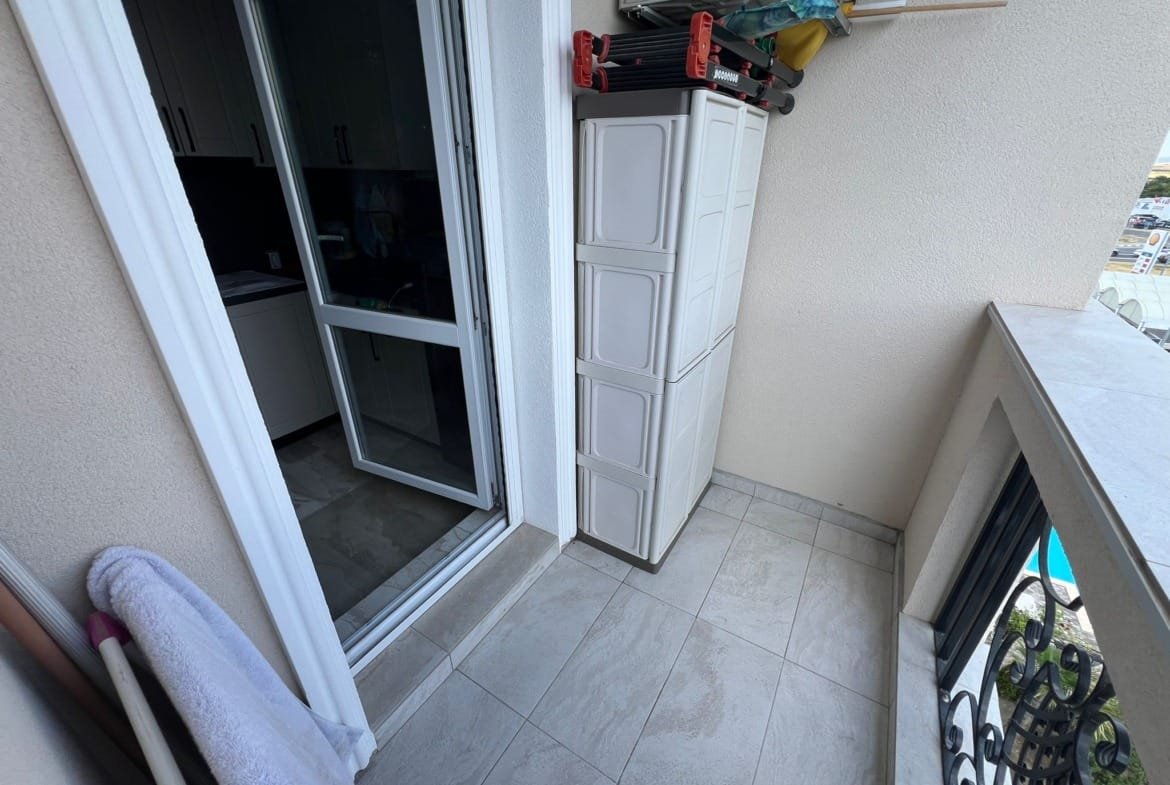 Балкон с плиткой, белым шкафом для хранения, открытыми дверями и видом на улицу, подходит для жизни и покупки недвижимости в Болгарии.