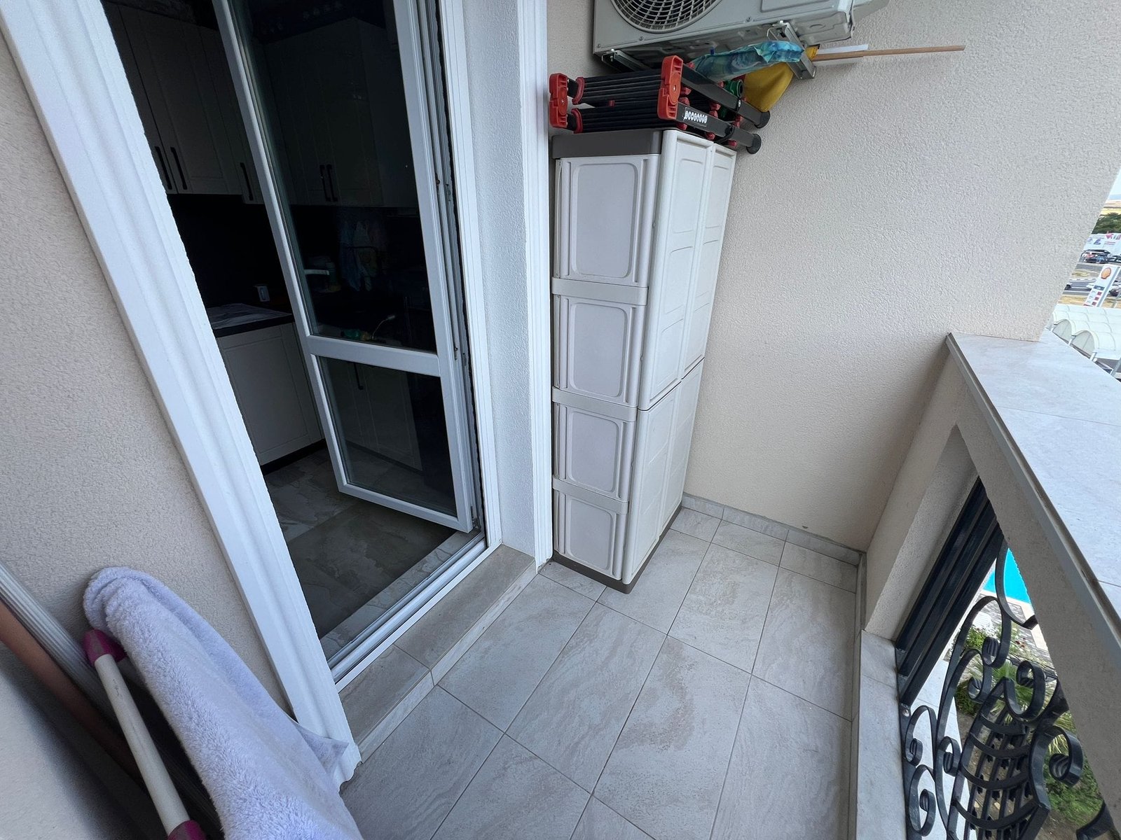 Балкон с плиткой, белым шкафом для хранения, открытыми дверями и видом на улицу, подходит для жизни и покупки недвижимости в Болгарии.