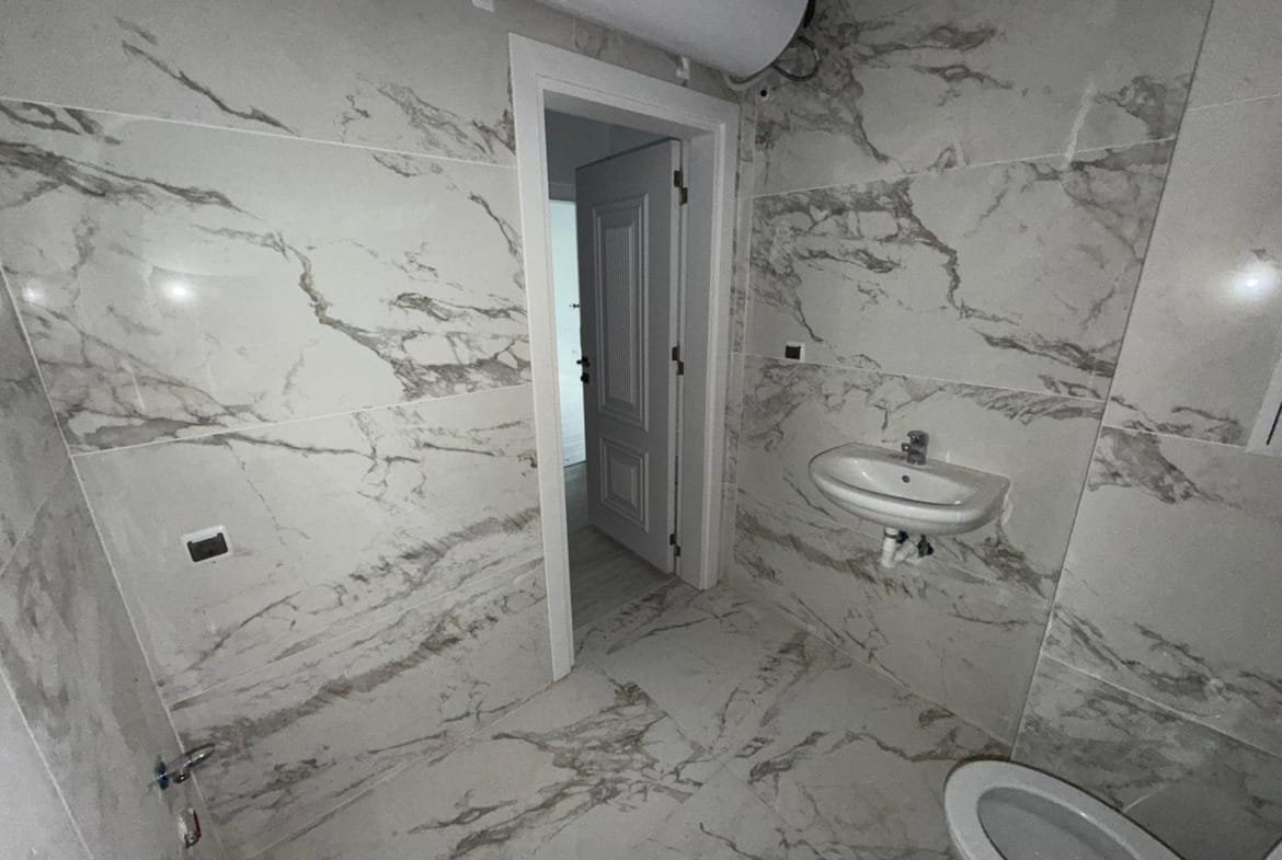 Современная ванная комната с мраморными стенами, умывальником и туалетом, идеально подходит для покупки недвижимости в Болгарии.