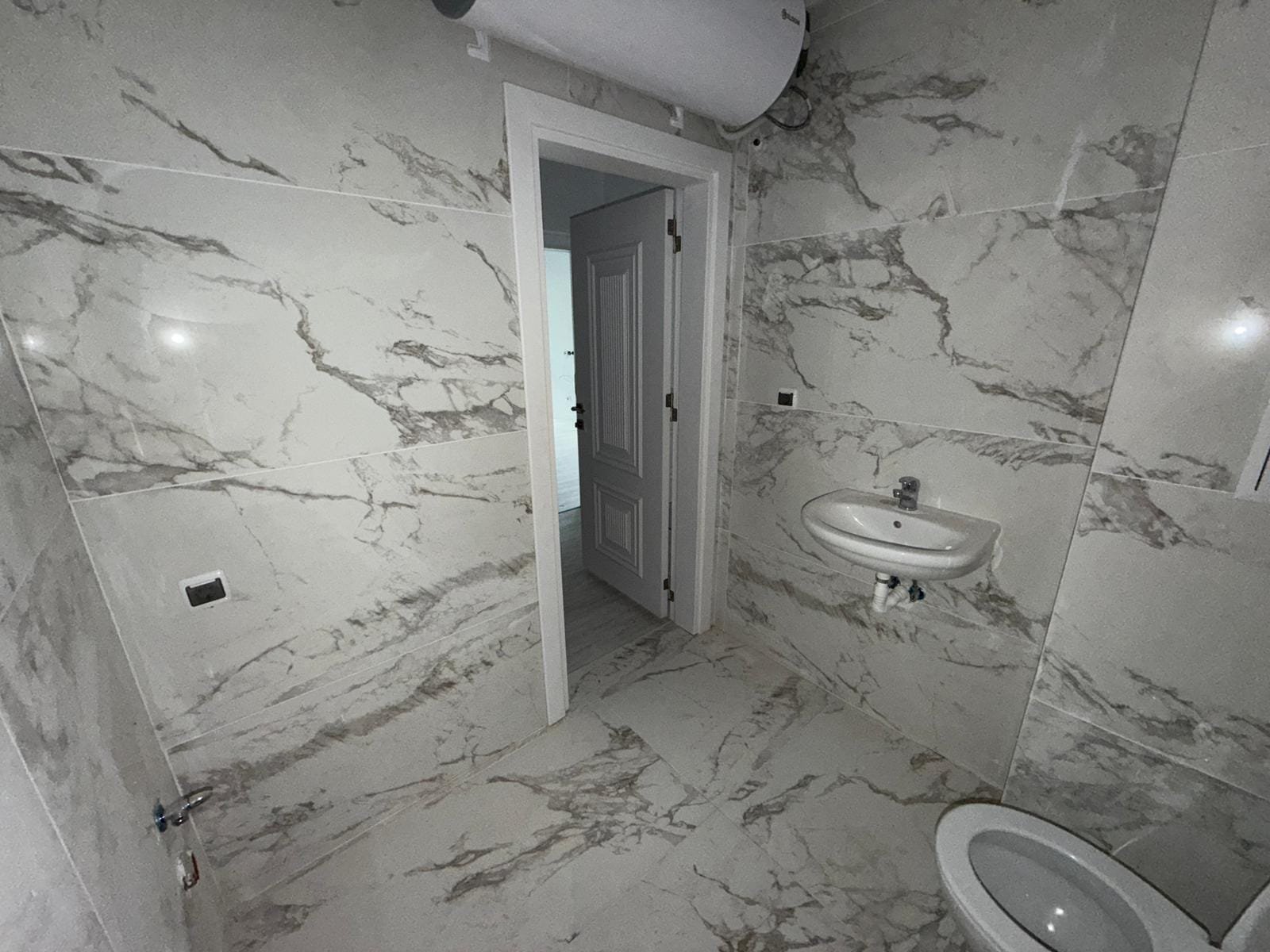 Современная ванная комната с мраморными стенами, умывальником и туалетом, идеально подходит для покупки недвижимости в Болгарии.